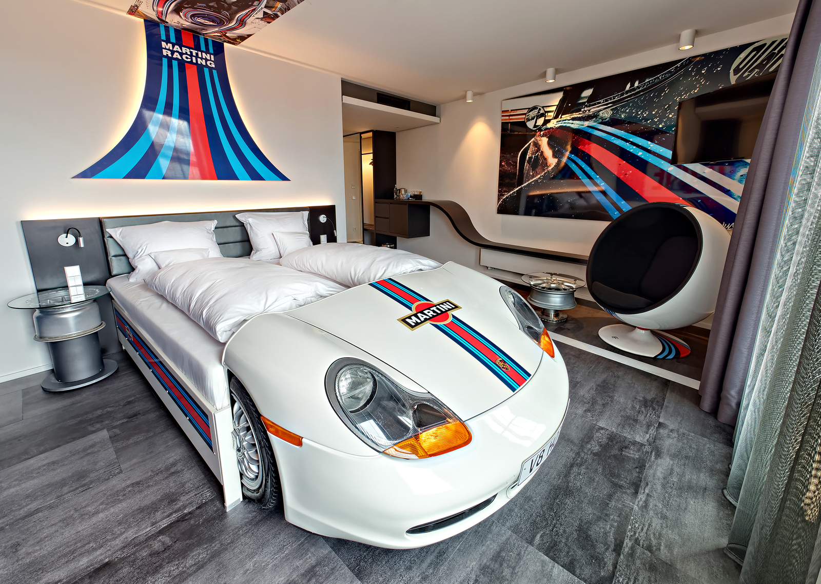 Autozimmer Petrol Heads mit weißem Autobett, Martini Racing Logos an den Wänden und dem Bett sowie ein großer Sessel.